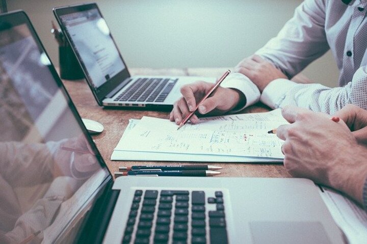 two people discussing a plan on paper sitting next to a computer